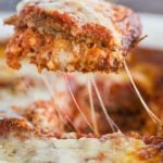 A slice of eggplant parmesan being lifted out of the pan.