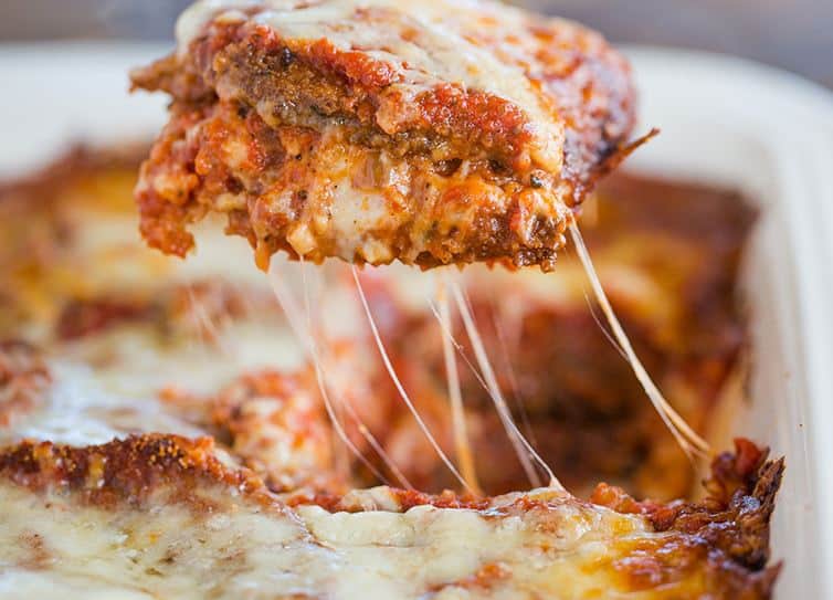 A slice of eggplant parmesan being lifted out of the pan.