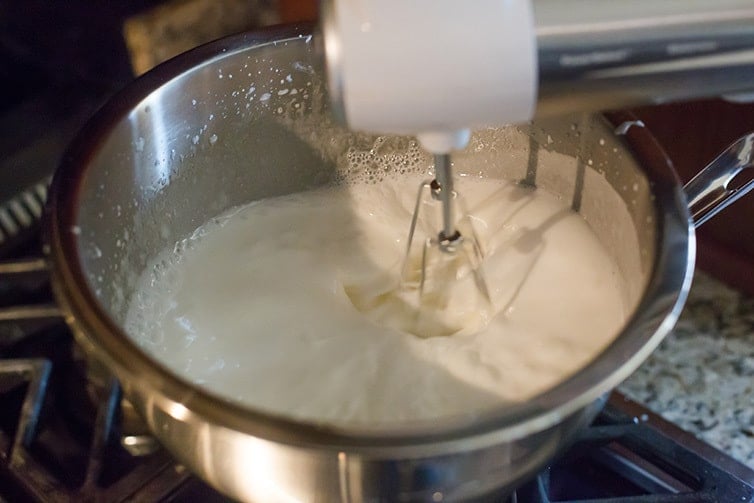 Beating 7 minute frosting in a bowl with a hand mixer.