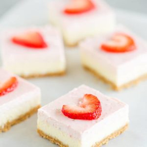 Five strawberry cheesecake bars on a piece of parchment paper.