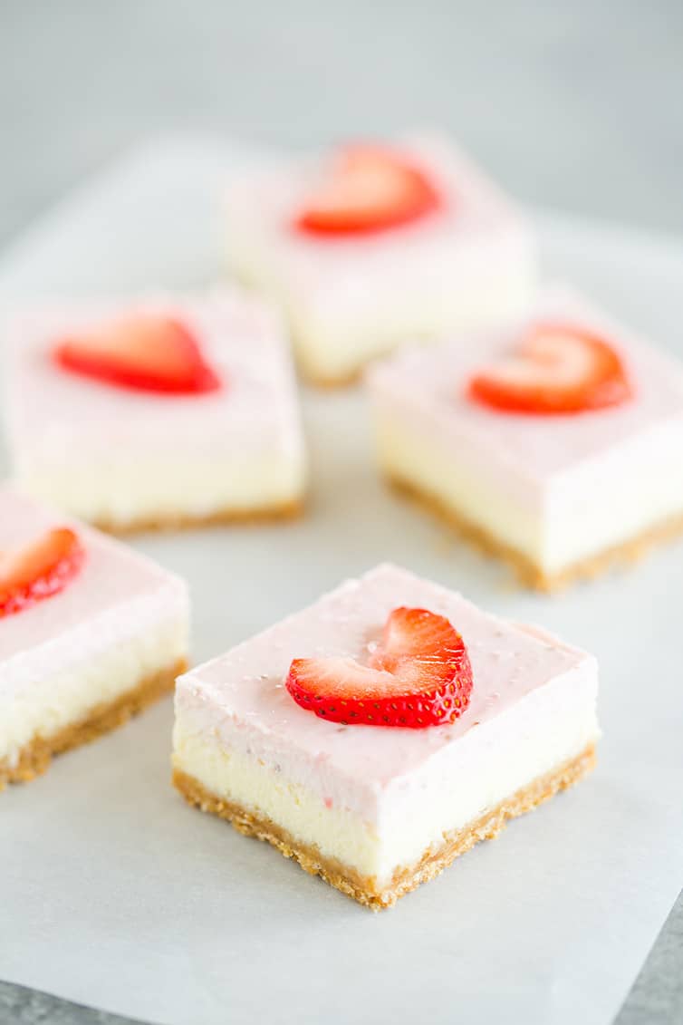 Five strawberry cheesecake bars on a piece of parchment paper.