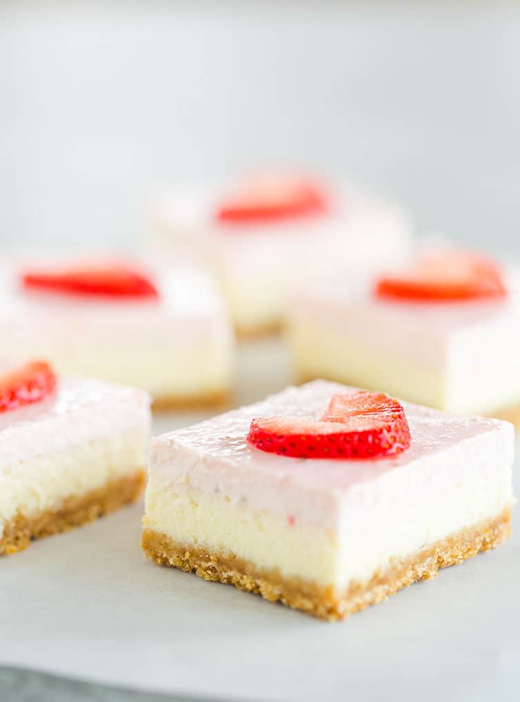 Multiple strawberry cheesecake bars sitting on parchment paper.