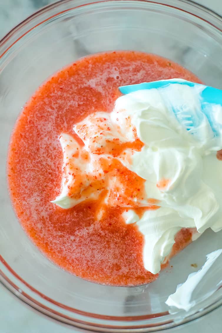 Strawberry puree being mixed with sour cream in a glass bowl.