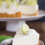 A slice of key lime cheesecake on a plate in front of the whole cheesecake.