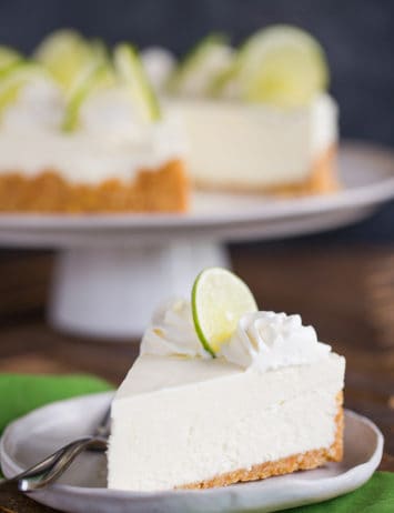 A slice of key lime cheesecake on a plate in front of the whole cheesecake.