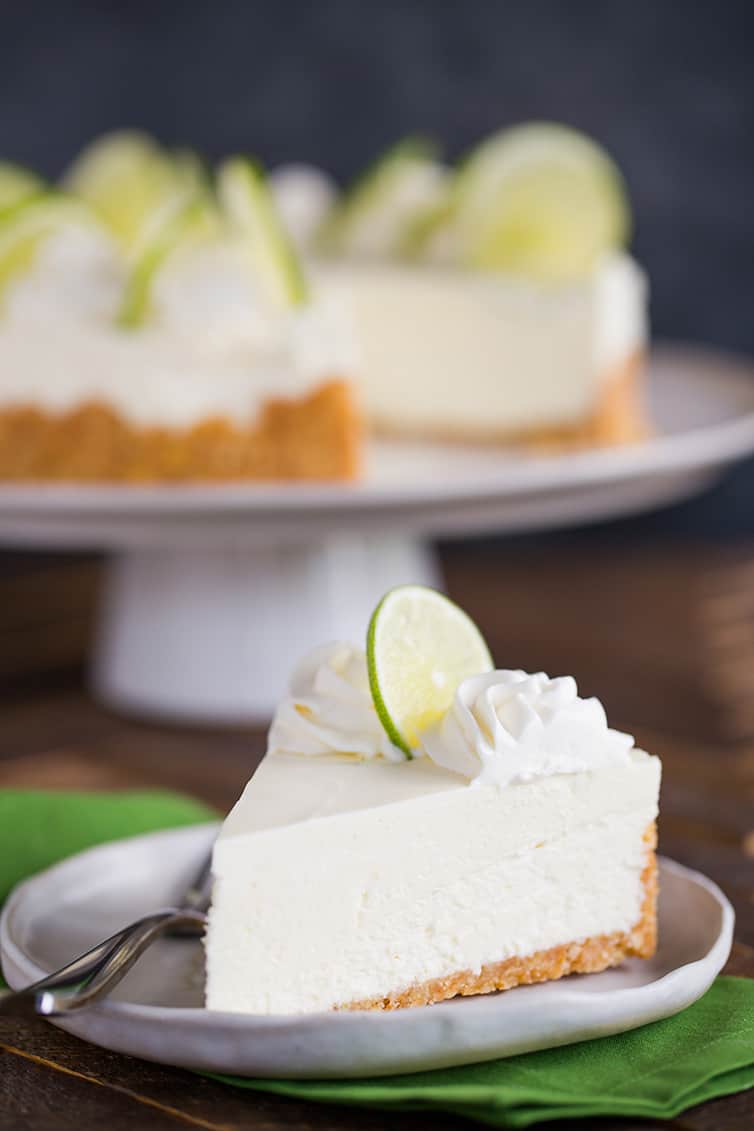 A slice of key lime cheesecake on a plate in front of the whole cheesecake.