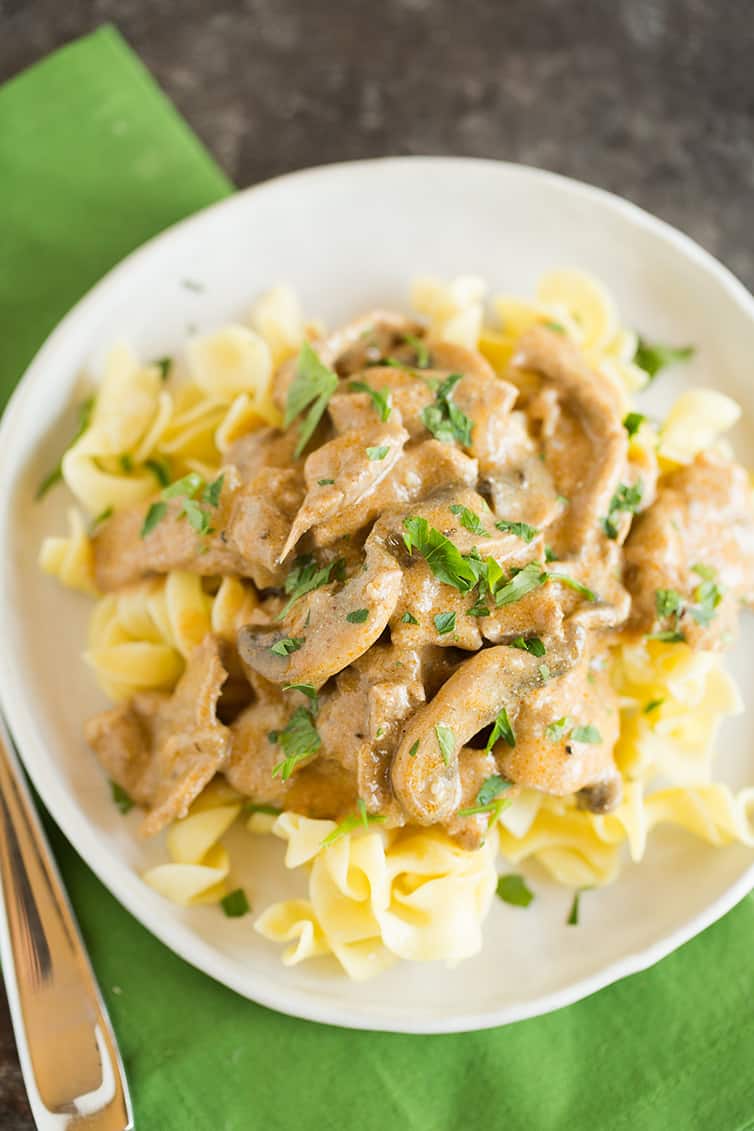 An overhead photo of a plate of beef stroganoff with a green napkin.