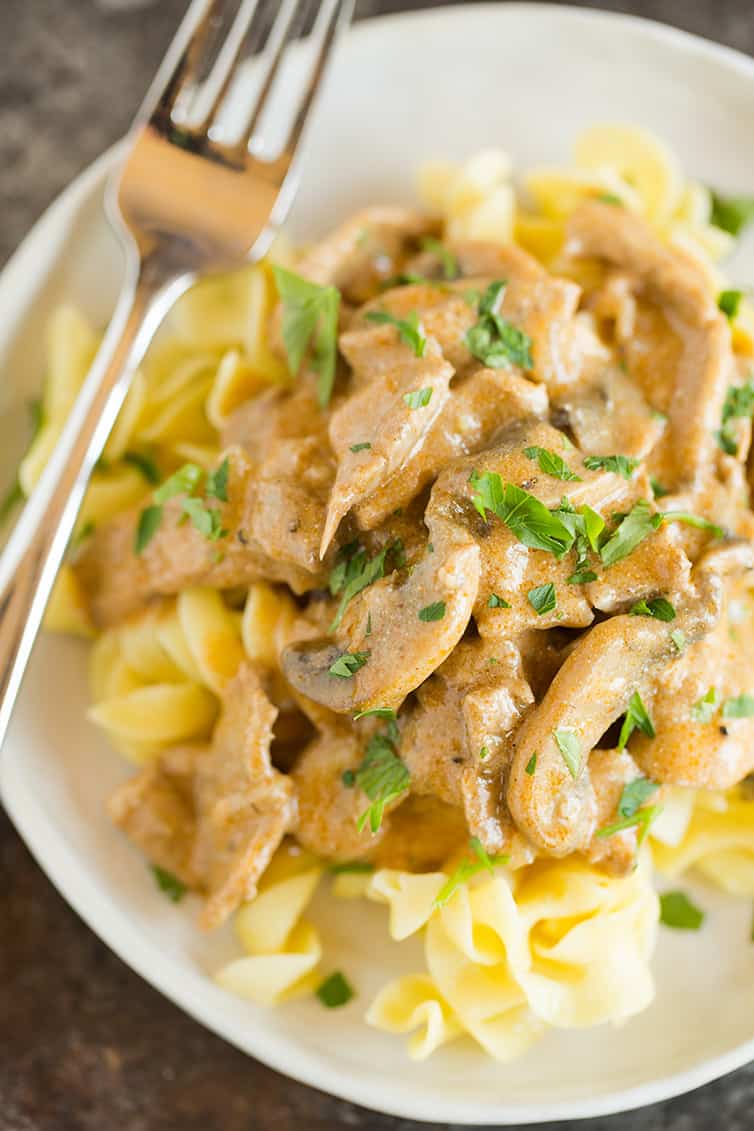 A plate of beef stroganoff over egg noodles with parsley sprinkled on top.