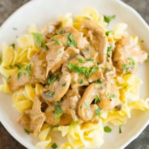 A plate of beef stroganoff over egg noodles.