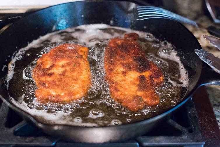 Chicken cutlets being pan-fried in a cast iron skillet.