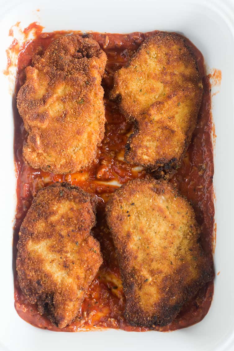 Four chicken cutlets in a pan on top of sauce.