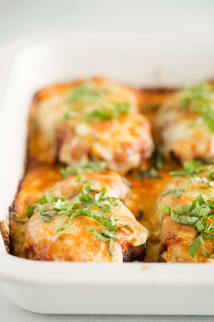 A pan with four pieces of chicken parmesan topped with fresh basil.
