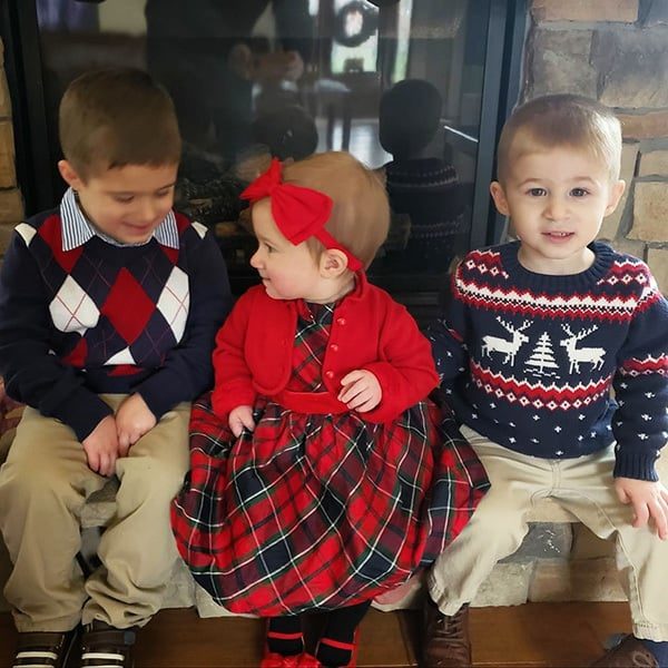 Two toddler boys and a baby girl sitting on the hearth of a fireplace.