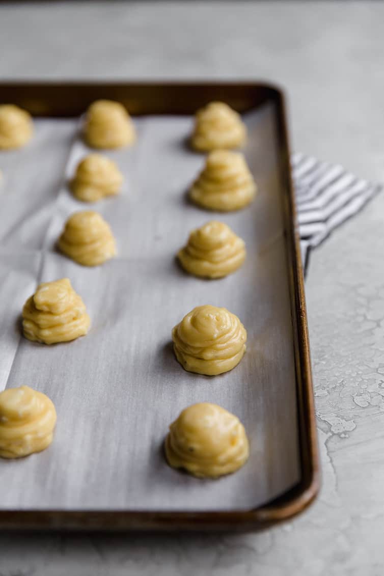 Gougeres dough piped into mounds on a baking sheet.
