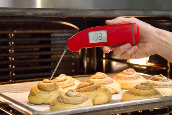A tray of cinnamon rolls with an instant-read thermometer inserted into one of them.