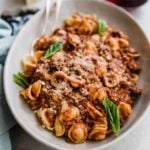 A bowl of pasta with bolognese sauce and fresh basil leaves.