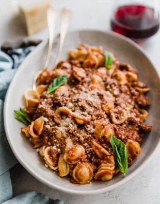 A bowl of pasta with bolognese sauce and fresh basil leaves.