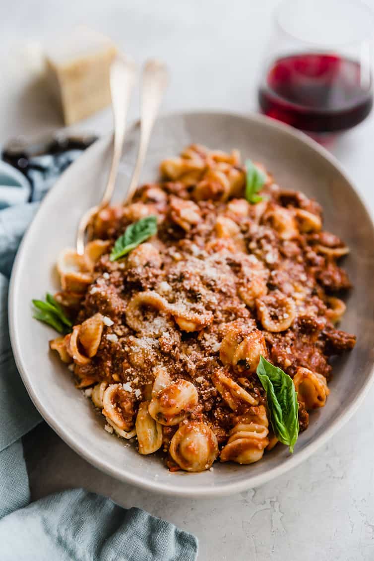 A bowl of pasta with bolognese sauce and fresh basil leaves.