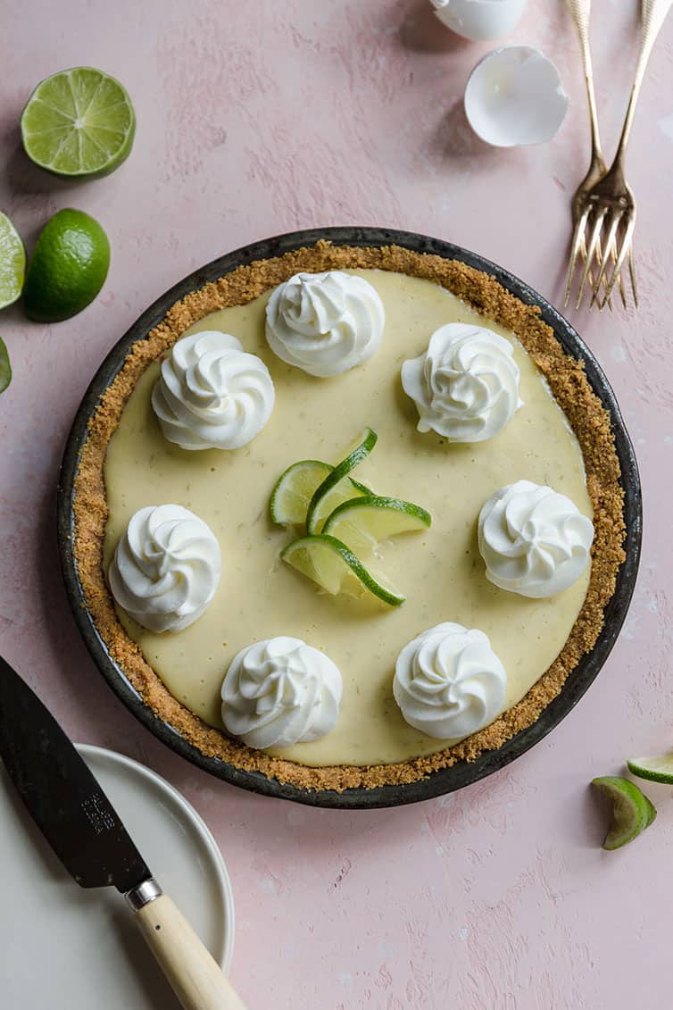 An overhead photo of key lime pie with whipped cream rosettes and lime garnishments.