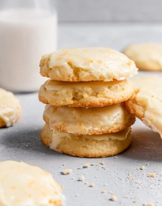 A stack of orange cookies with a glass of milk in the background.