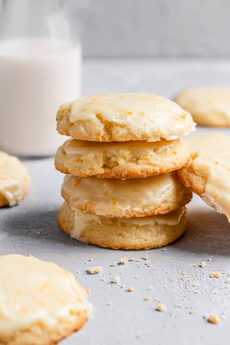 A stack of orange cookies with a glass of milk in the background.