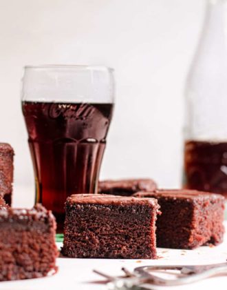 Pieces of chocolate cake in front of glasses of Coca Cola.