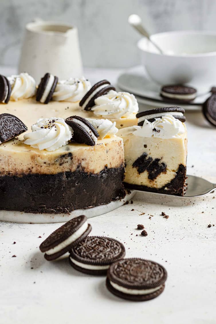 Oreo cheesecake with a slice coming out and Oreo cookies on the counter.