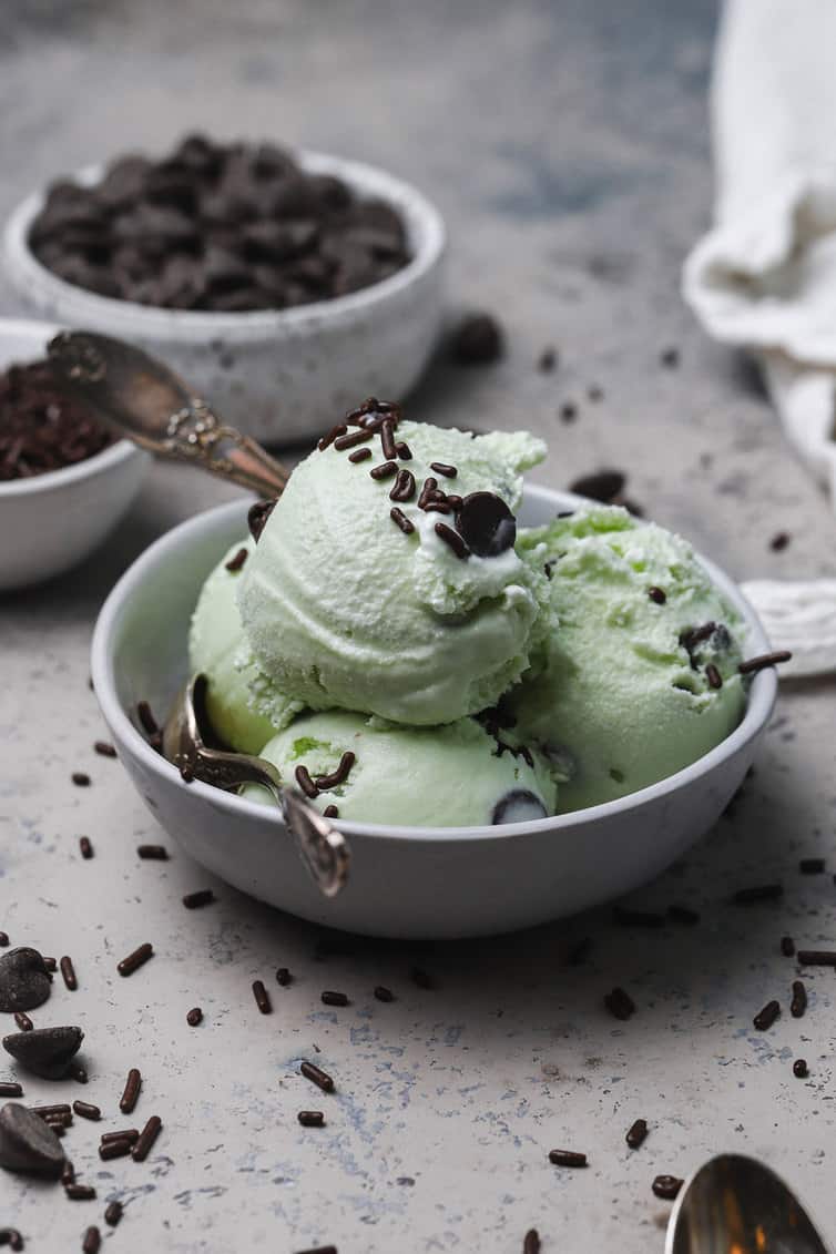 Four scoops of mint chocolate chip ice cream in a bowl with chocolate sprinkles.