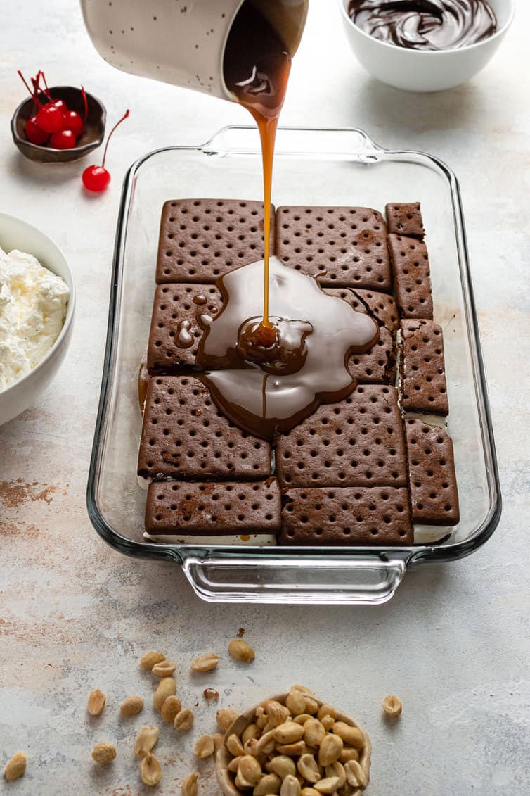 Drizzling caramel sauce over ice cream sandwiches in a glass baking dish.
