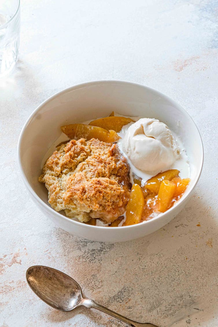 A bowl of peach cobbler with vanilla ice cream.