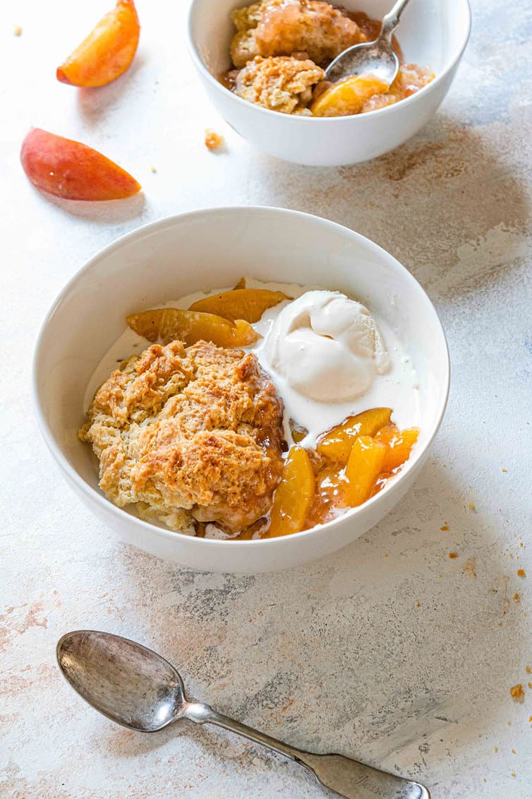Two bowls of peach cobbler with vanilla ice cream.
