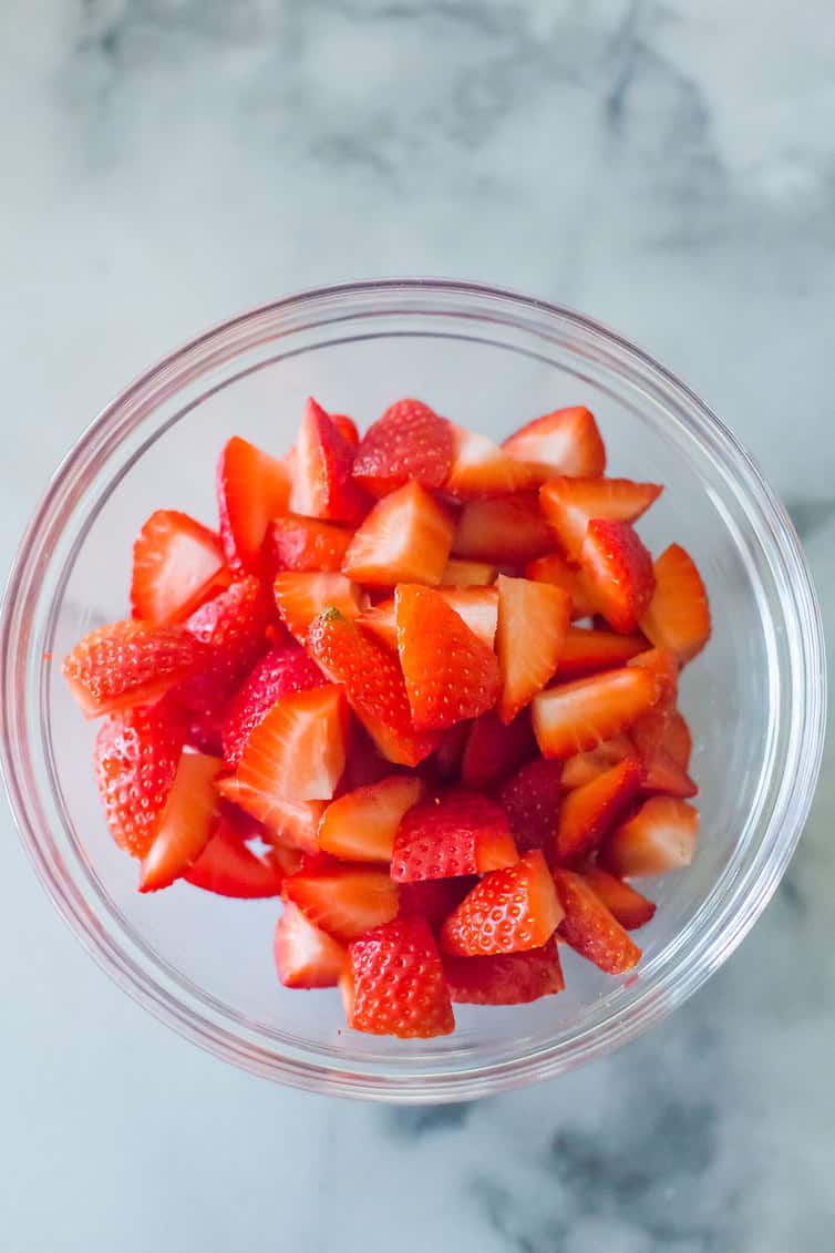 A glass bowl full of quartered strawberries.