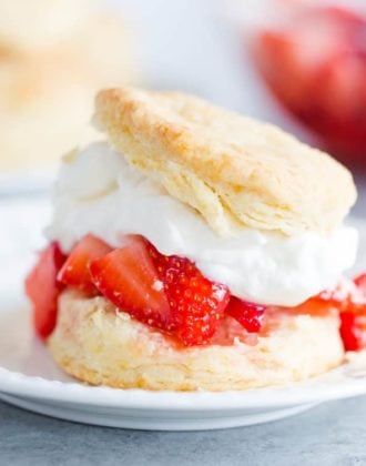 A biscuit filled with strawberries and whipped cream on a white plate.