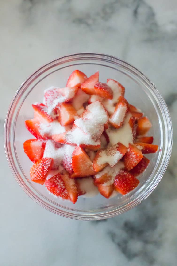 Strawberries in glass bowl sprinkled with sugar.