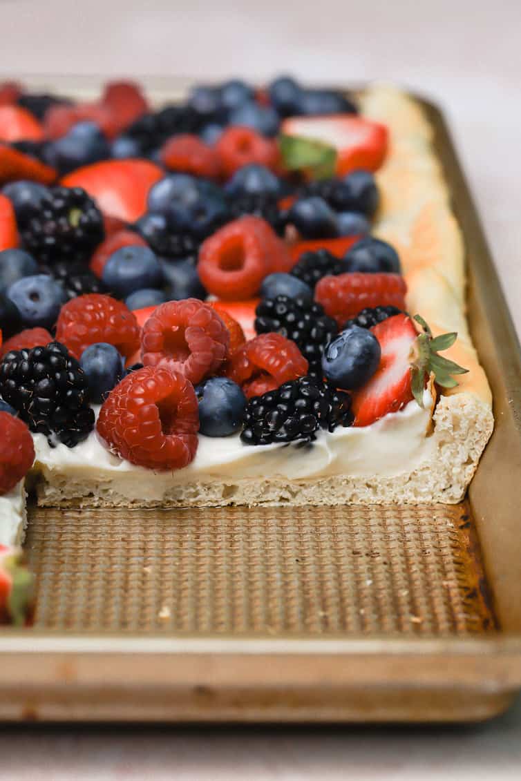 Fruit pizza cut with a large piece removed in the pan.