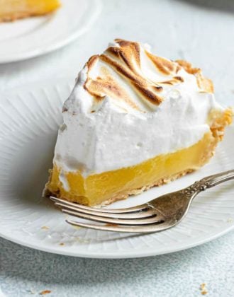 A slice of lemon meringue pie on a white plate with a fork.