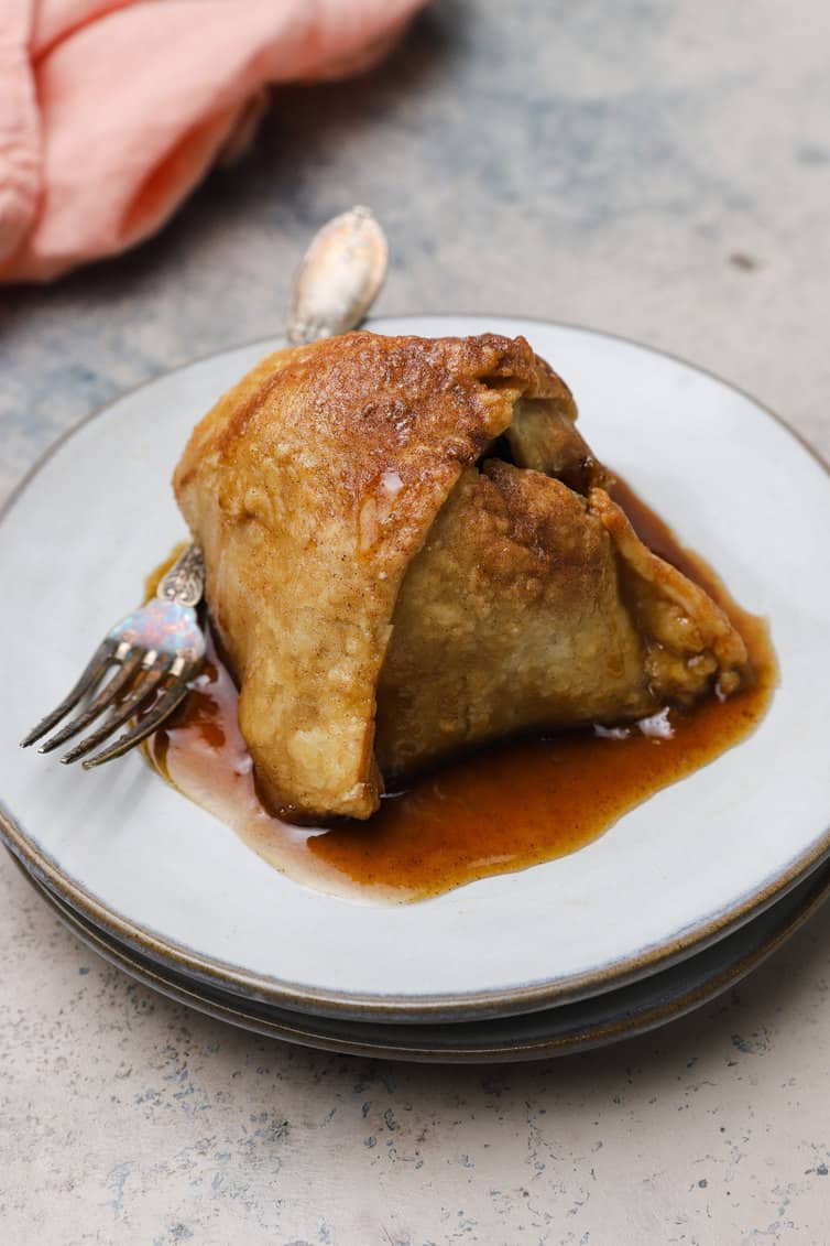 A baked apple dumpling on a white plate with a fork.
