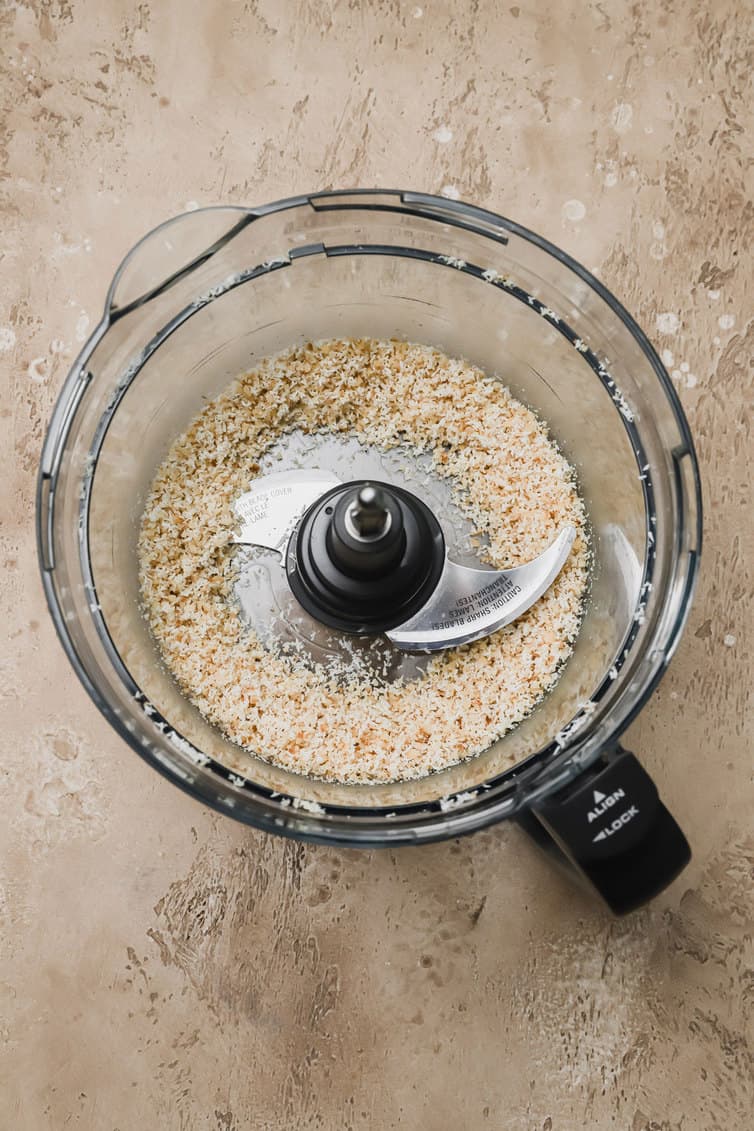 Coconut and walnuts ground together in a food processor bowl.
