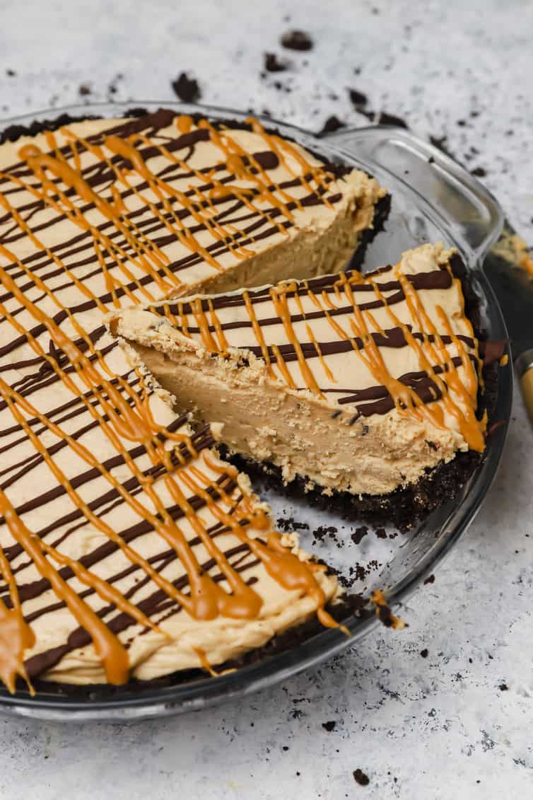 Peanut butter pie in a glass pie plate with a slice cut out.