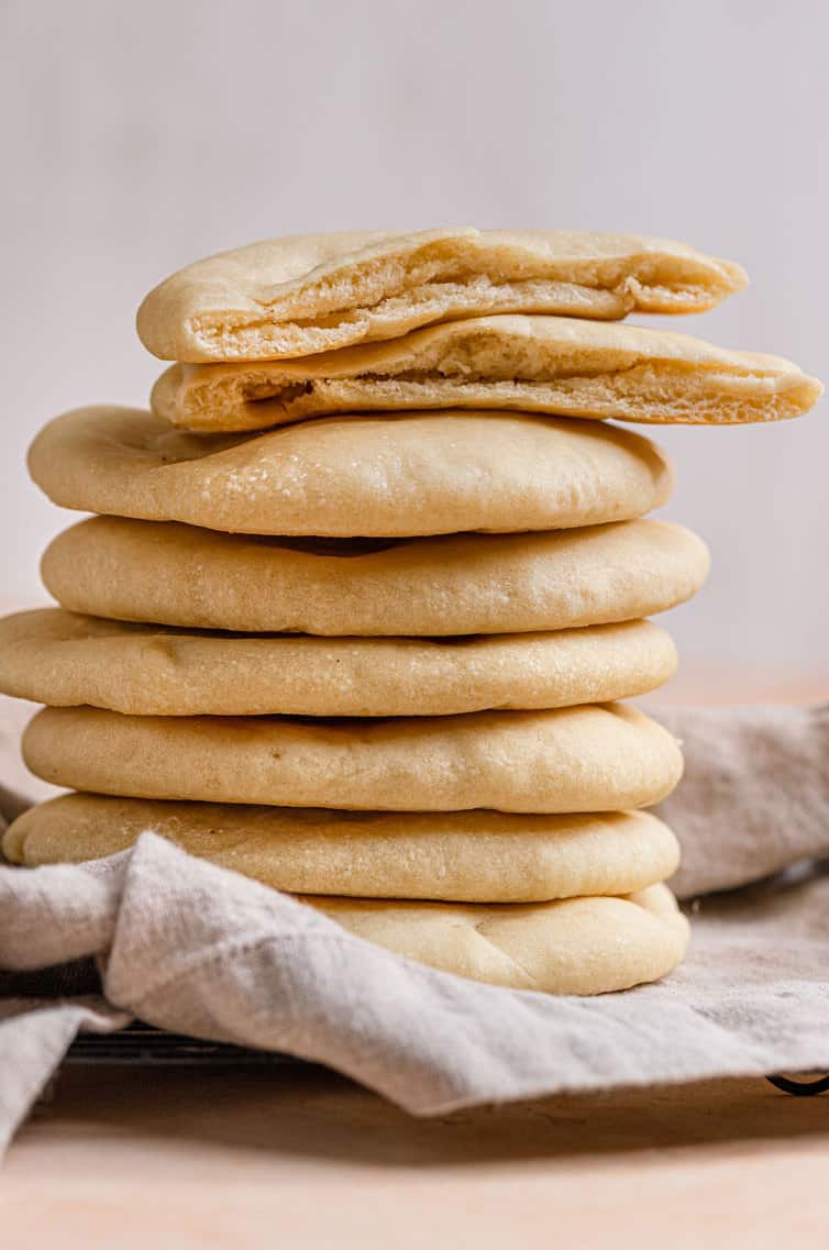 A stack of pita bread with one cut in half on top.