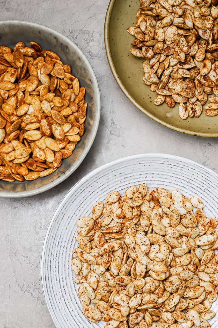 Three bowls of roasted pumpkin seeds with different spice blends.