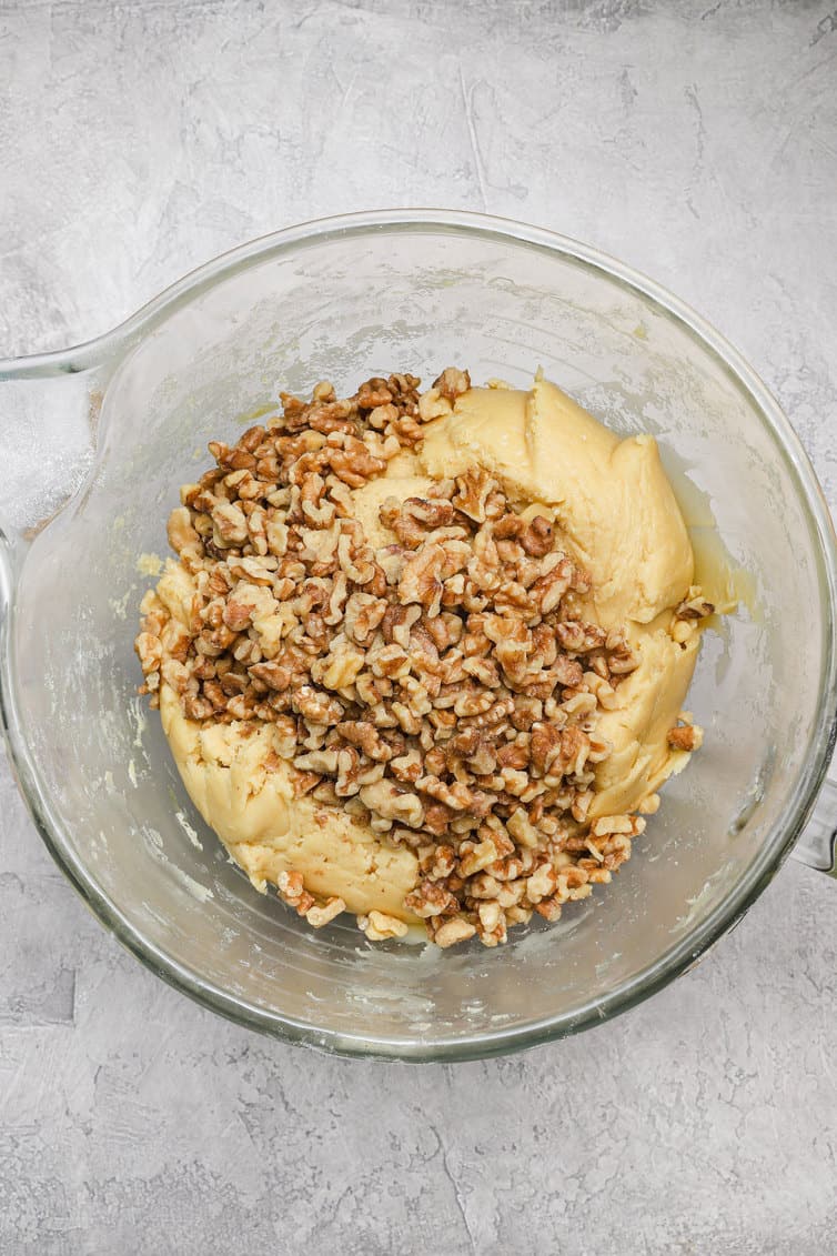 Biscotti dough in a glass bowl with chopped walnuts.