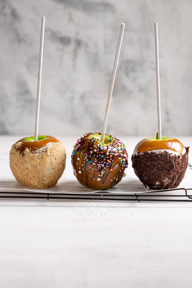 Three caramel apples in a row with different garnishes on them.