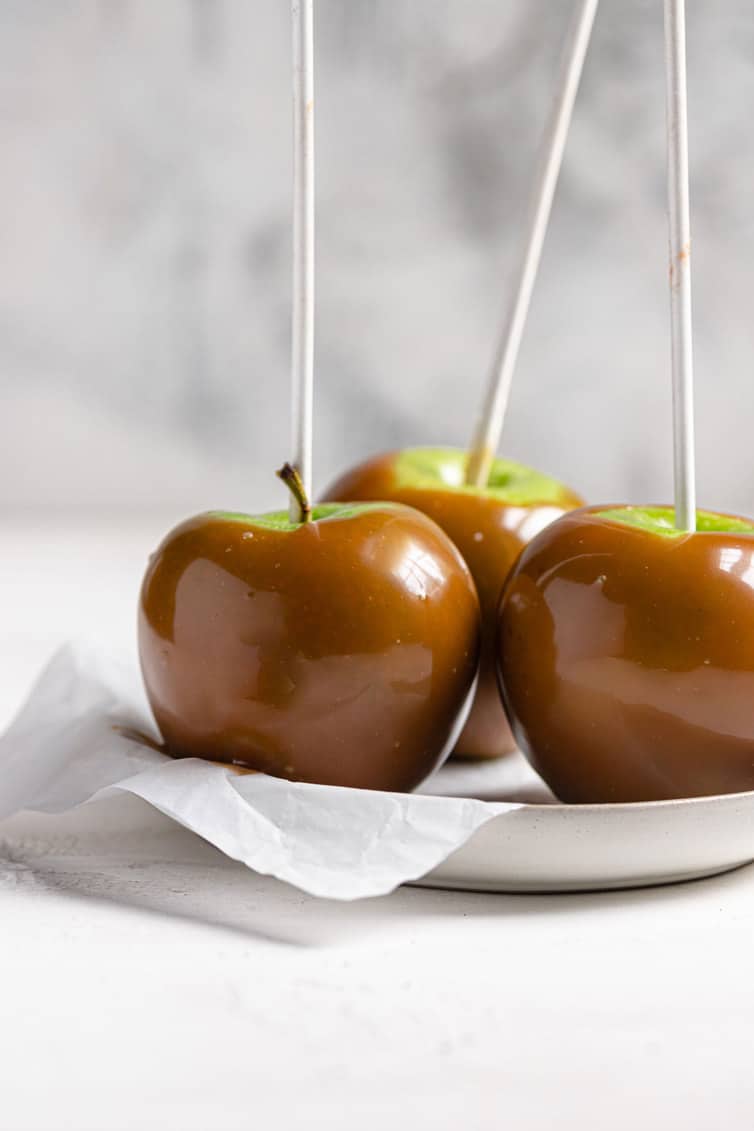 Three caramel apples on parchment paper on a white plate.
