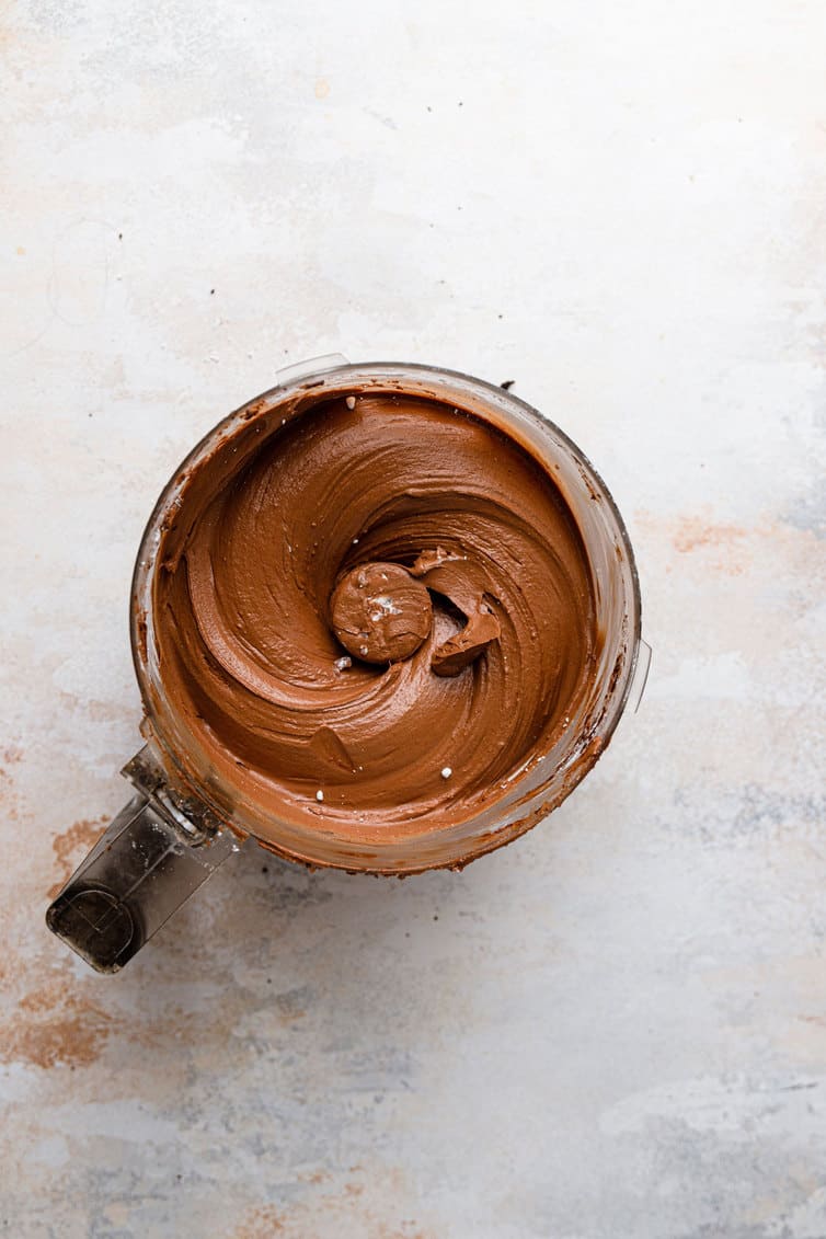 Chocolate fudge frosting in the bowl of a food processor.