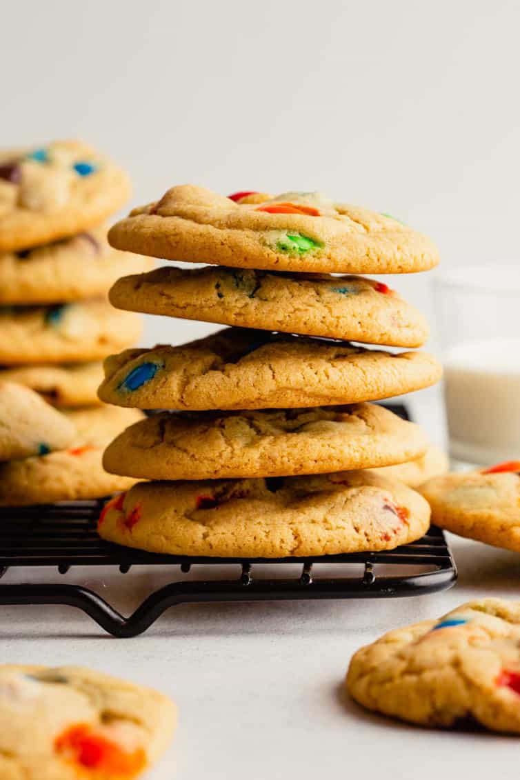 A stack of M&M cookies on a cooling rack.