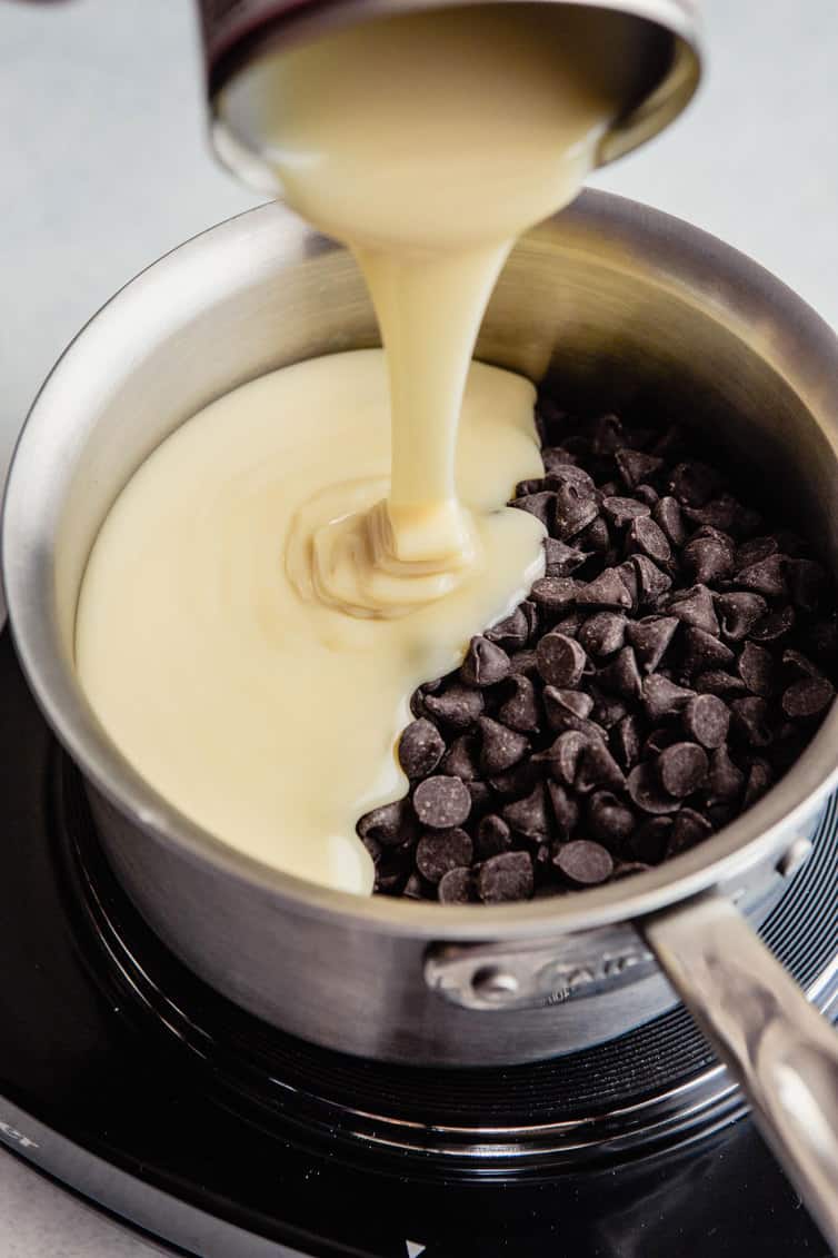 Pouring sweetened condensed milk into pan with chocolate chips.