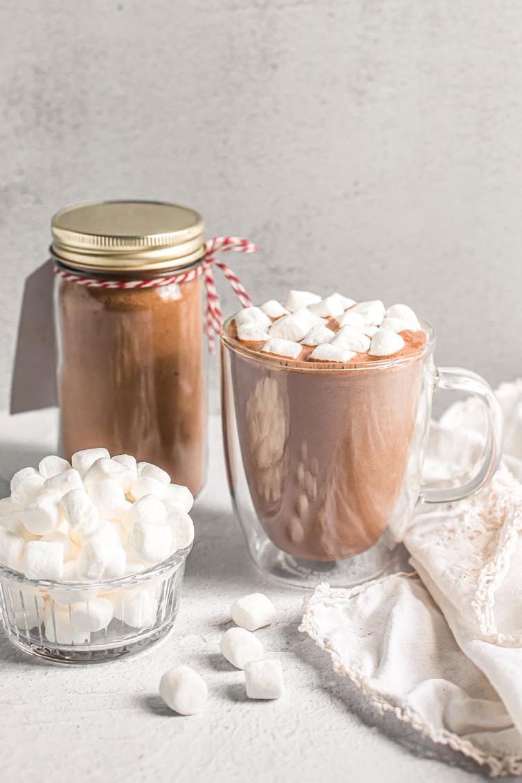 Cup of hot chocolate and mini marshmallows with mix in background.