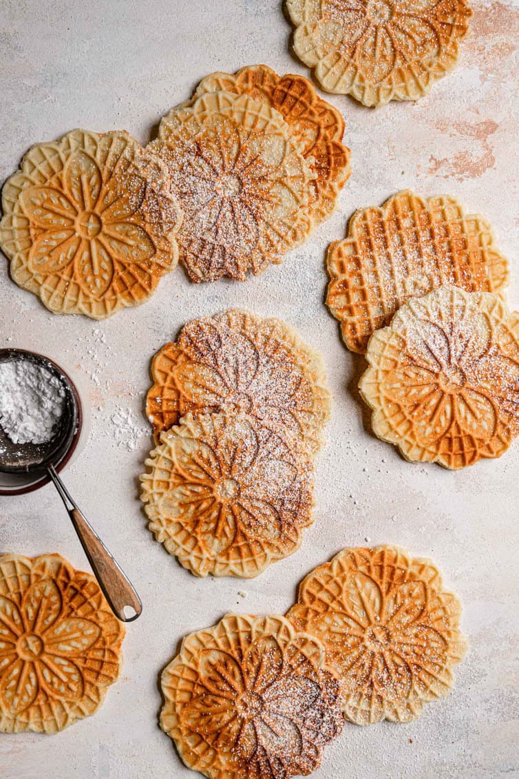 Pizzelle dusted with powdered sugar on a flat surface.