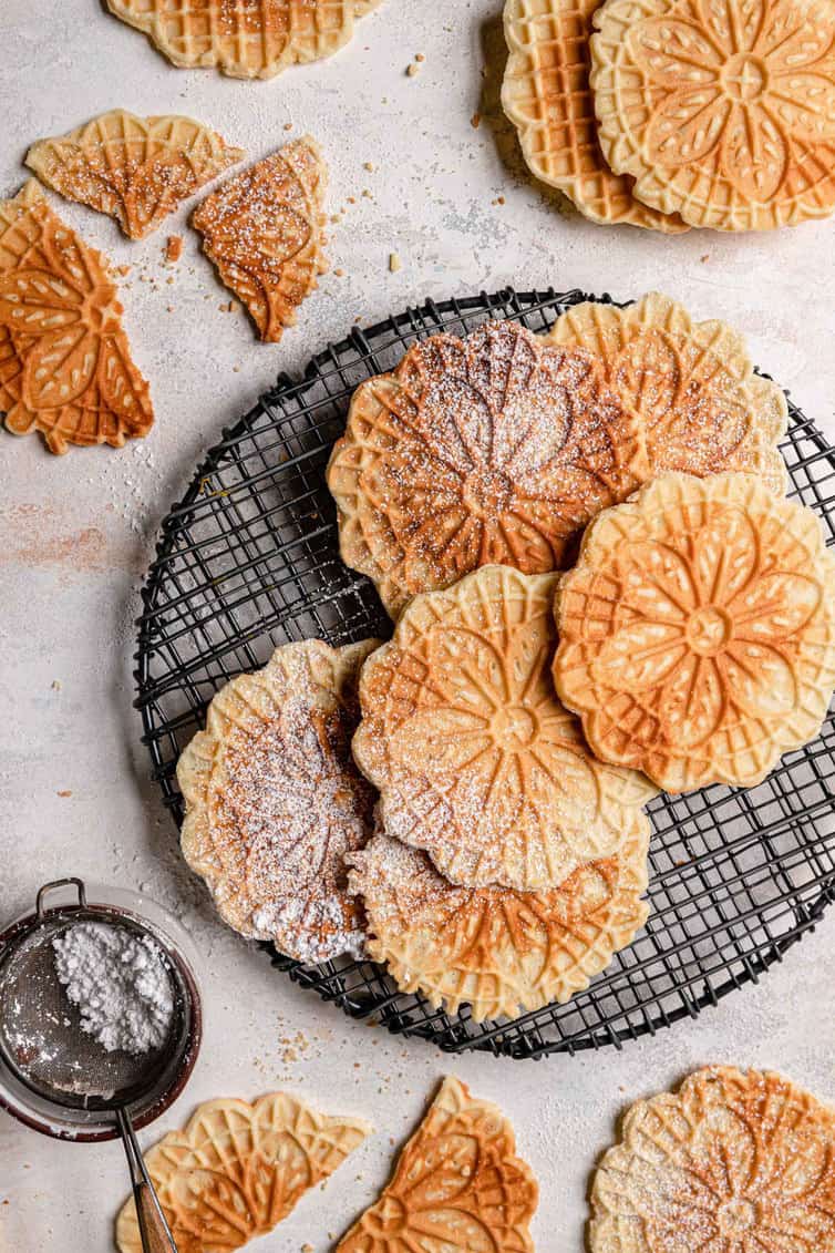 Overhead photo of pizzelle on cooling rack, some dusted with powdered sugar.